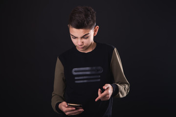 a boy in a black T-shirt is looking in his phone, angry or upset at the gimmick or news, showing...