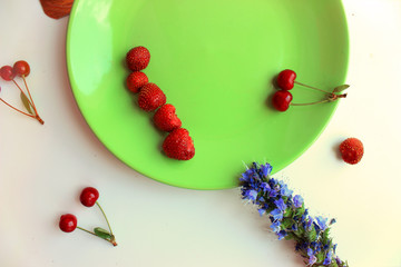 Summer season. Vitamins cherries and strawberries on green plate. Wildflowers. Copy space
