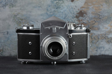 The old 35 mm SLR camera on a grey cement wall.