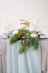 Beautiful decorated table with plates for guests, blue candles, pine decoration and flowers and wedding cake on the table in studio