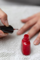 Woman coating her finger nails with red enamel on a white towel in the bathroom