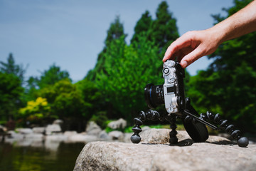 Photograph male hand handling an old vintage camera on tripod in front of water pond in Planten un Blomen Park Hamburg, Germany