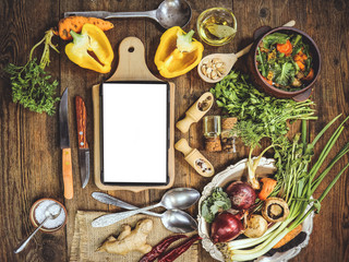 Ingredients for cooking a spring dish with vegetables, mushrooms and dandelions. tablet computer on the kitchen table. place for text. wooden background.