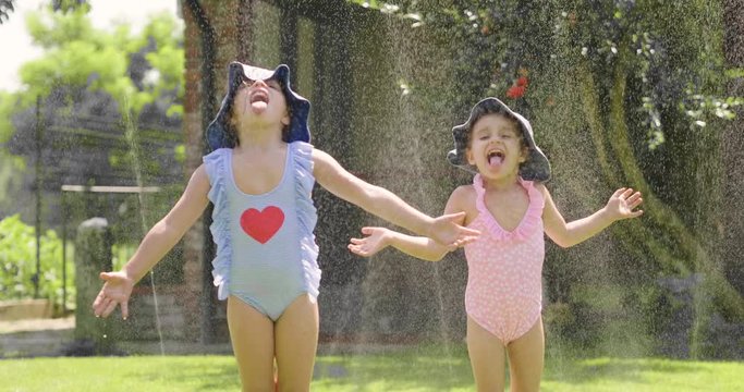 Two little girls play in the garden with water, the two girls run, get wet and laugh. Concept of: family, love, fun and happiness.
