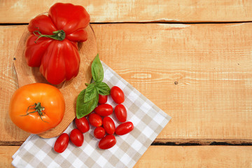 Large red tomato, yellow tomato, cherry tomatoes and basil with a cloth on a wooden background