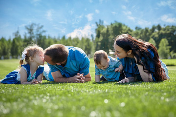 Cheerful family in a park, parents and their two children are lying on the grass. Shot with flare