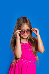 Portrait of young pretty girl in pink dress, sunglasses and hat on blue background . Summer vacation and travel concept