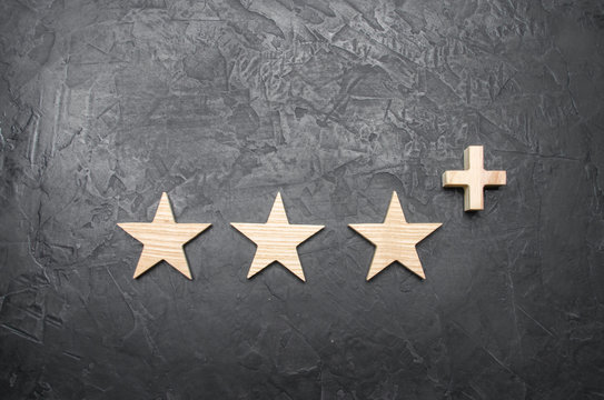 Three wooden stars and a plus, on a concrete gray background. The concept of the highest evaluation of quality and service. Better than five stars. Excellent performance and stunning success.