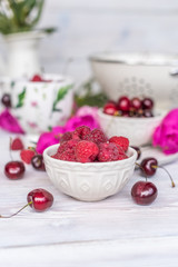  raspberries, cherries and strawberries in bowls, flavors of summer with peony flowers