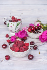  raspberries, cherries and strawberries in bowls, flavors of summer with peony flowers