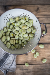 broad beans in a white colander on a wooden table