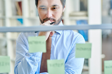 Pensive formal man in office composing sticky notes and thinking on project for business...