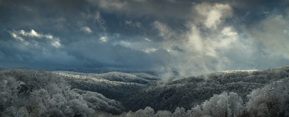 Fränkische Schweiz -Panorama eines Waldmittelgebirges bei dramatischem Himmel mit einfallender Sonne im Winter mit Schnee