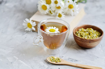 Cup of tea with chamomile flowers on gray background, book reading, free time concept