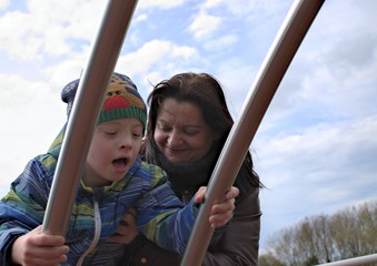 Defect,childcare,medicine and people concept- happy mother and son with down syndrome  playing in a playground.