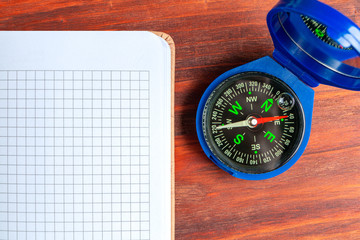 A compass and a blank notebook on wooden background