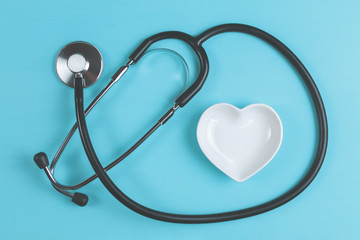 Stethoscope and white heart-shaped saucer on turquoise wooden background