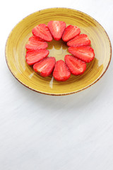 Strawberries on a yellow plate, red strawberry halves lined circle top view, red berries on a white background, vegetarian food for breakfast, copy space, blank for the designer