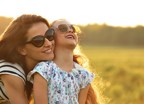 Happy fashion kid girl embracing her mother in trendy sunglasses and looking on nature background. Closeup portrait of happiness.