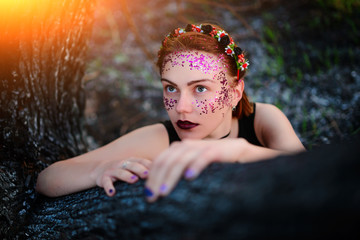 A young beautiful woman with a violet shine on her face sits near a burnt tree