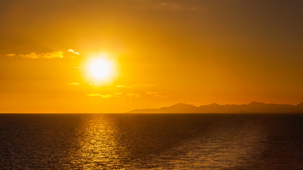 Fototapeta premium Lanzarote Sunset. Sunset over the coastline of the Spanish Canary island of Lanzarote. A yacht can be seen passing under the sun on the horizon.