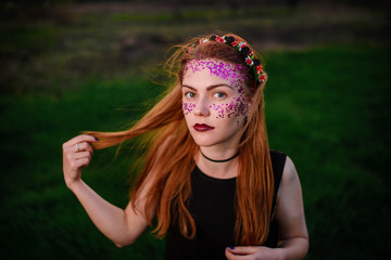 A young beautiful woman with a violet shine on her face standing on the grass and looking at the camera