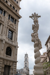 Fototapeta na wymiar Statue of a Pieta on a column with the Basilica de San Francisco de Asís (Basilica of San Francisco of Asis) in the Plaza of San Francisco, also known as Pigeon Square, in Old Town Havana, Cuba.