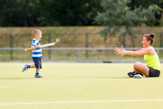 Small boy training playing field hockey with stick on the field with his mother