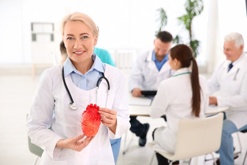 Obraz premium Female doctor holding heart model in clinic. Cardiology center