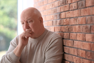 Senior man in state of depression near brick wall
