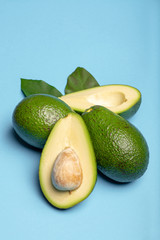 Fresh organic ripe green whole and sliced Fuerte avocado with leaves, copy space close up isolated on trendy blue background