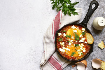 Shakshouka (spicy tomato stew with chicken eggs) with feta cheese - traditional dish of israeli cuisine.Top view with copy space.