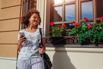 Beautiful college girl using smart phone and listening to the music by university