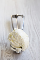 Ice cream in a spoon for ice cream over white wooden surface, close-up.