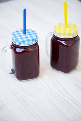 Side view, glass jars with berry smoothie over white wooden background.