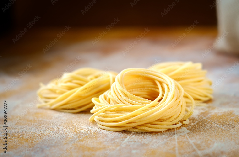 Wall mural raw homemade spaghetti nest with flour on a wooden table. fresh Italian pasta