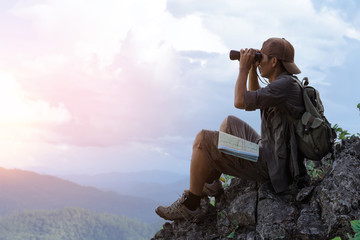 Young man with backpack and holding a binoculars sitting on top of mountain