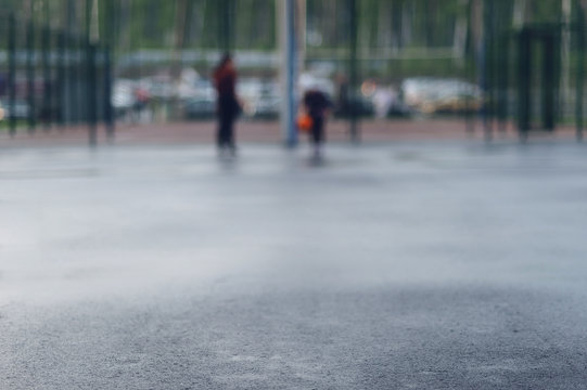 Wet asphalt in focus for text on the background of street basketball court on which people play