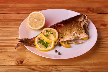 Appetizing baked fish, covered with juicy lemons, garlic and salt on side, above view