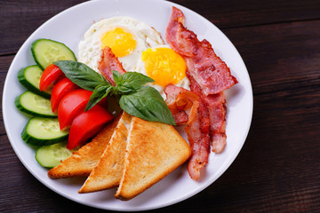Breakfast concept. European morning meals- fried eggs with bacon and toasts,served with fresh vegetables, healthy food with fat and proteins. Tasty and nutritional day starter