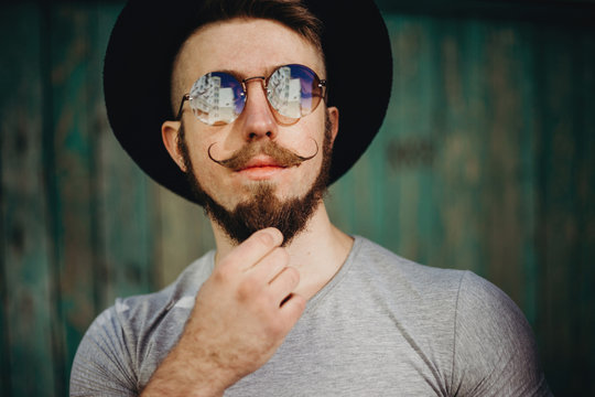 Bearded hipster in sunglasses and hat with fashionable mustaches. Fashion portrait of young male model. People, emotions, barbershop and style concept