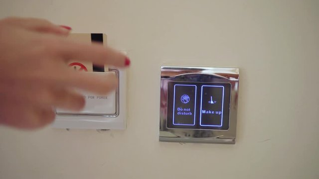 Closeup of woman inserting electronic key card in power switch holder on wall in the hotel. Then push the button does not disturb on the smart touch screen.