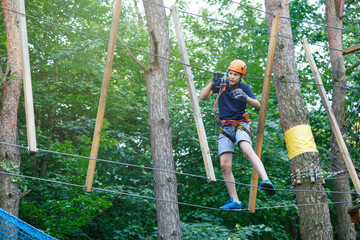 Active sporty kid in helmet doing activity in adventure park with all climbing equipment. Active children climb on the trees and having fun outdoors. Summer camp.