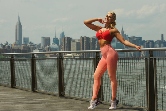 Attractive young woman with sexy fit body in bright sportswear enjoying sunny day on the pier.