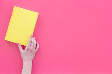 Reading concept. Reading as hobby. Hands take hardback book with empty cover on pink background top view copy space