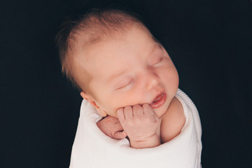 newborn baby sleeping wrapped in white scarf on black background