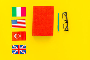 Language study concept. Textbooks or dictionaries of foreign language near flags on yellow backgrond top view copy space