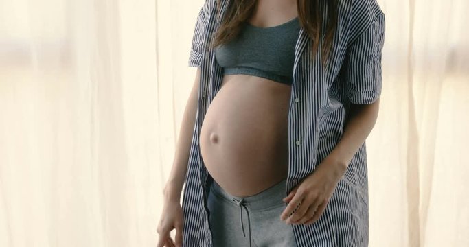 Crop faceless view excited pregnant woman in expectancy wearing top and hat and dancing emotionally having fun at home alone