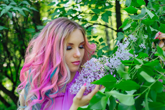 Beautiful girl with colorful dyed hair and perfect makeup and hairstyle standig next to lilac bush
