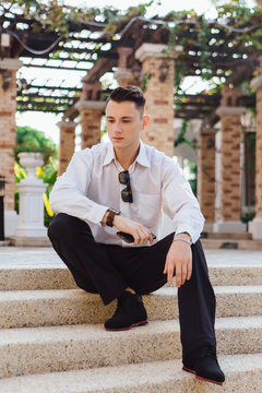 Young businessman holding his phone and sitting on stairs outdoors